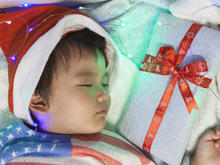 サンタクロースの帽子をかぶったまま眠る男の子の枕元に置かれたプレゼントの包み紙